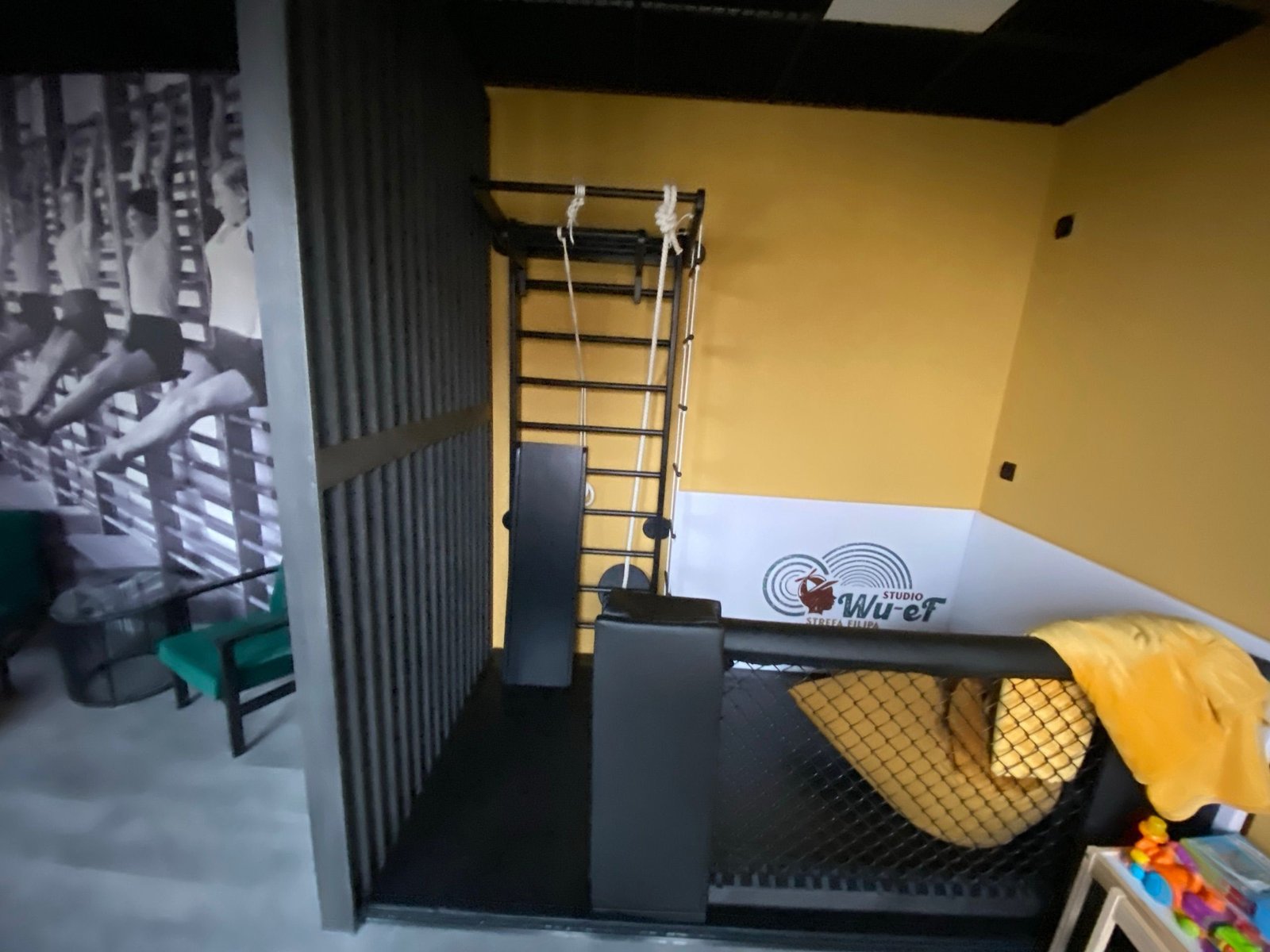 Panel z siatką MMA i drabinka gimnastyczna przy logo Studio Wu-eF w strefie dziecięcej