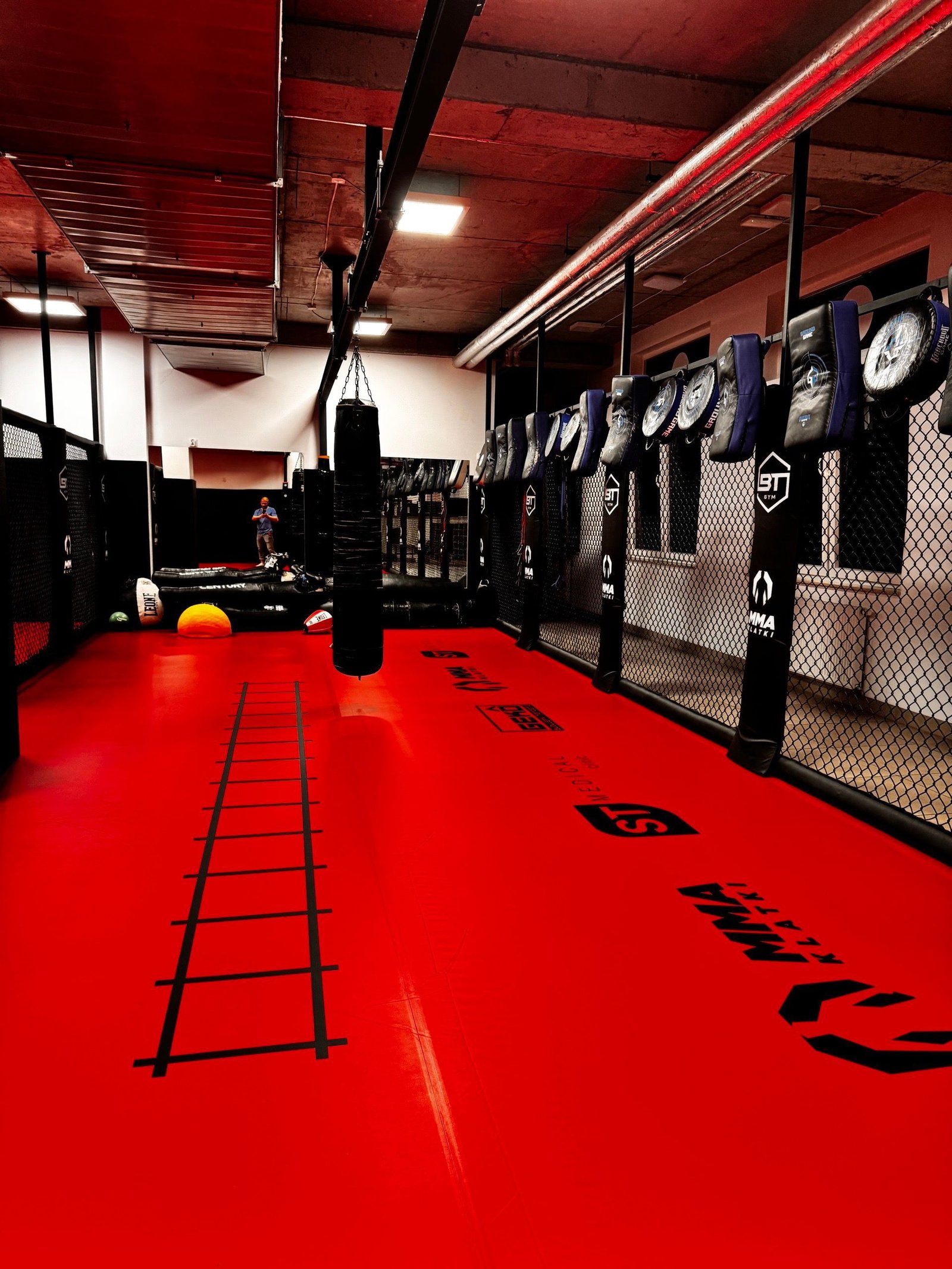 Klatka MMA z obszyciami BT Gym, czerwona mata i tarcze treningowe zawieszone na konstrukcji