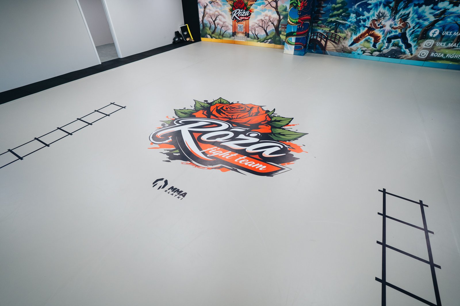 Duże logo Róża Fight Team nadrukowane na jasnej macie podłogowej. Po bokach widać pola do pracy nóg, a w tle personalizowane maty ścienne.