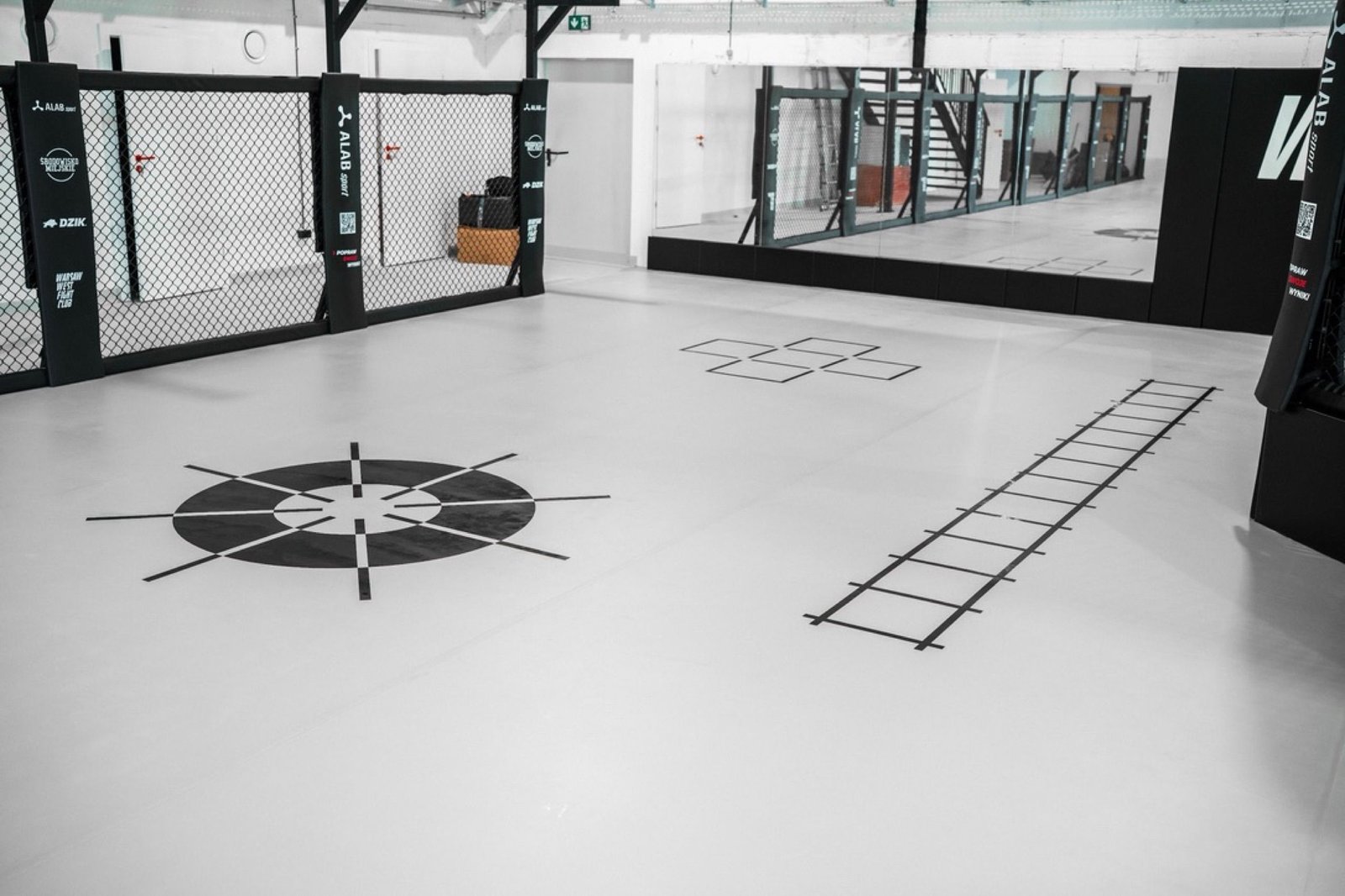 Grafiki treningowe na jasnej macie przy zabudowie luster i klatce Warsaw West Fight Club