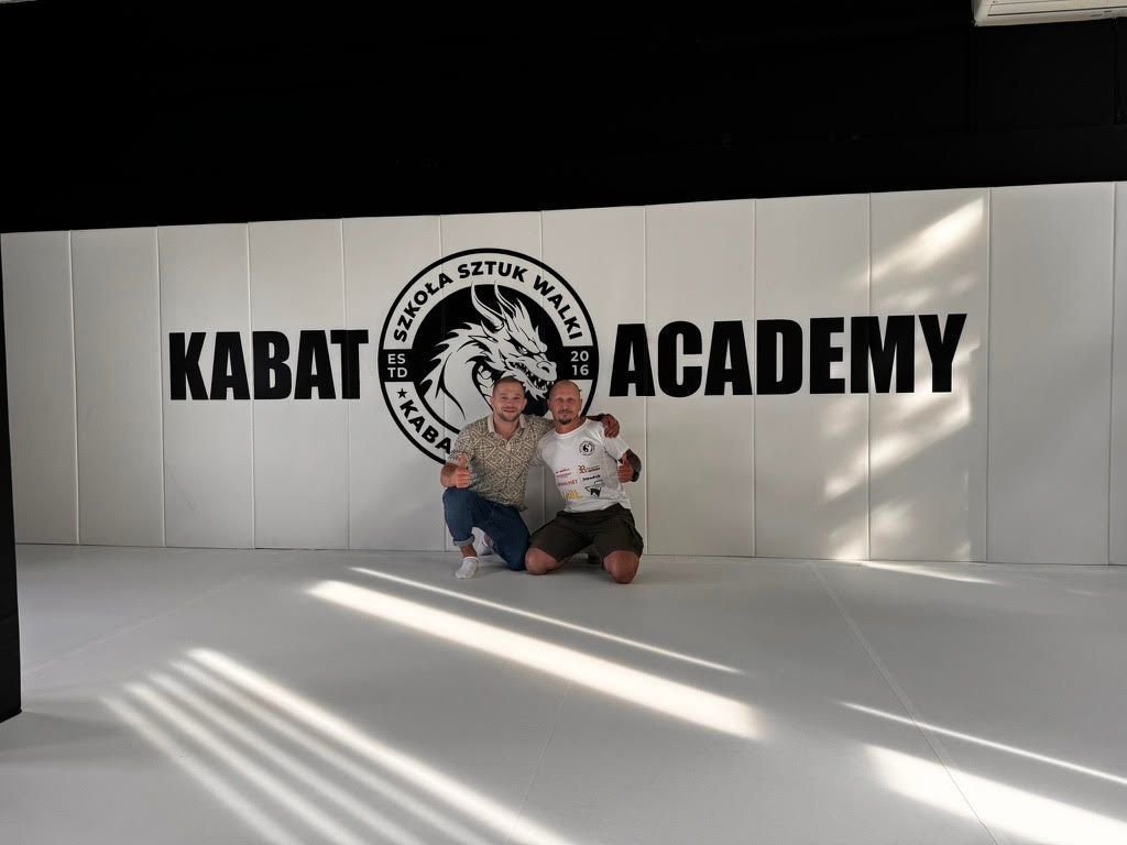 Białe maty ścienne z czarnym logo Kabat Academy, dwóch mężczyzn na białej macie podłogowej
