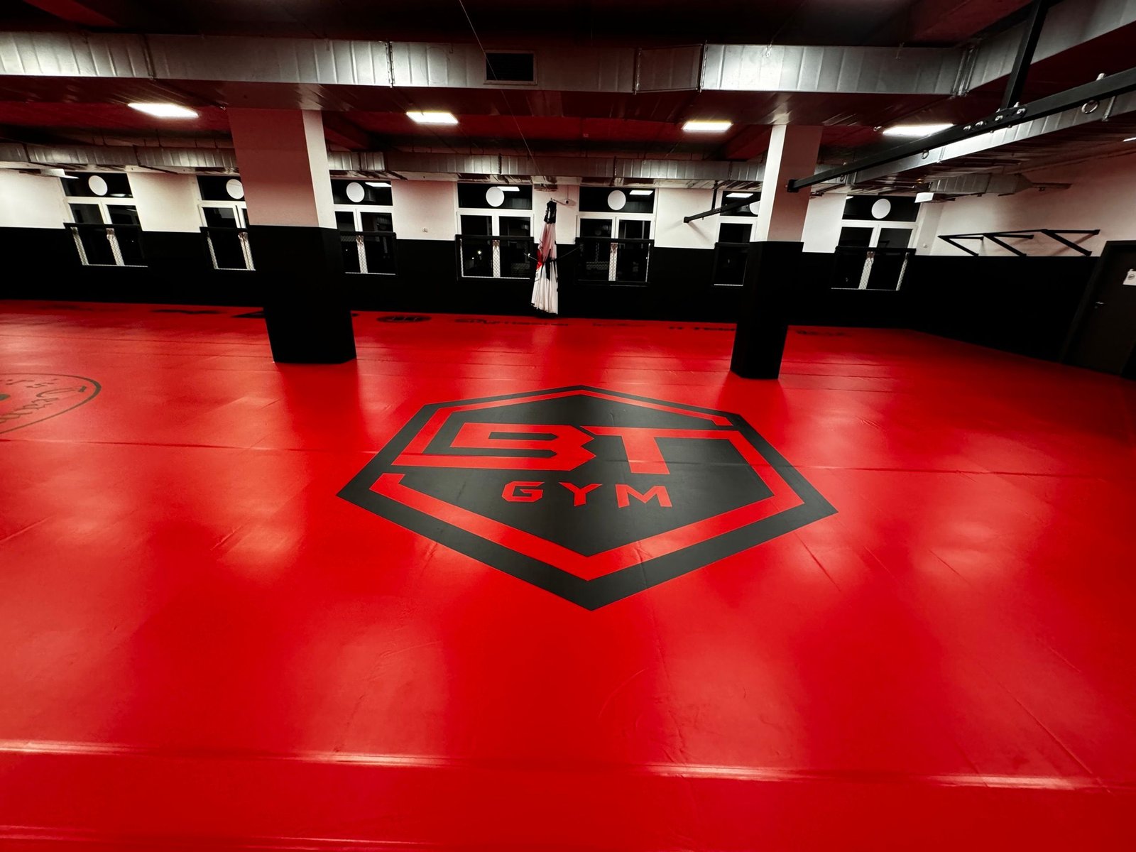 Czerwona mata z logo BT Gym oraz drążki do podciągania na ścianie sali Open Space