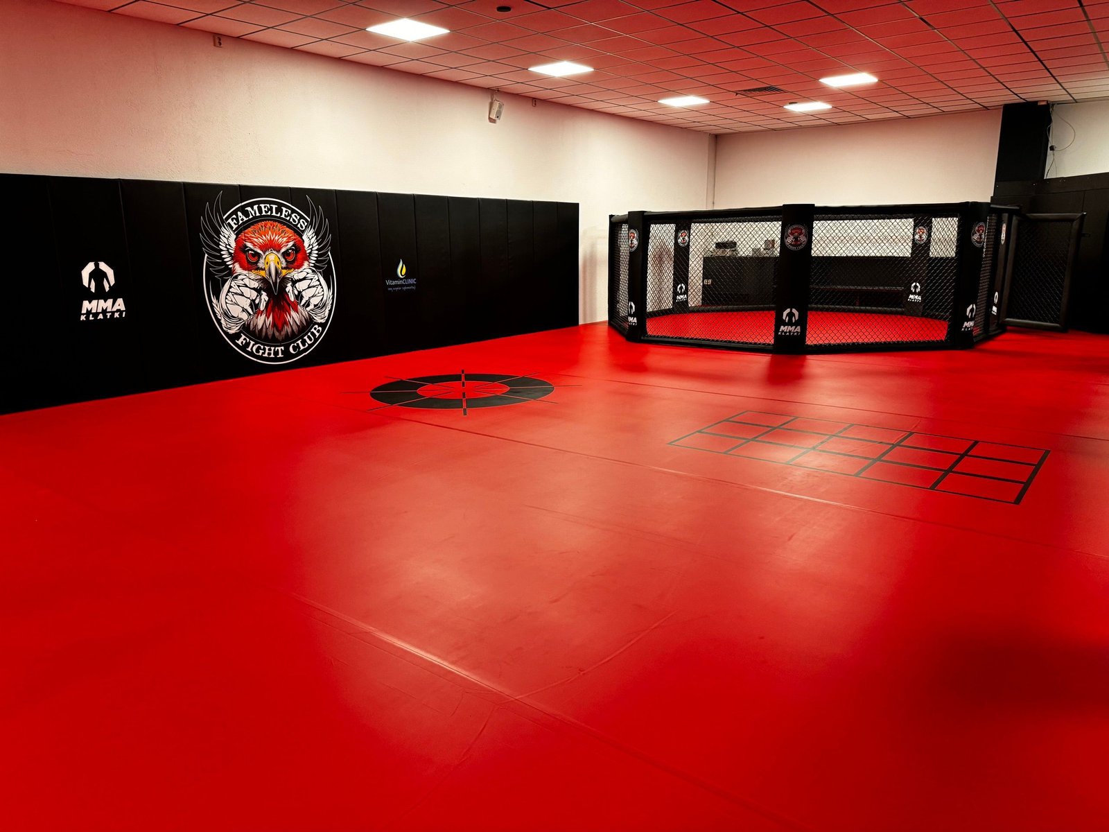 Czerwona mata treningowa Fameless Fight Club z czarnymi matami ściennymi z logo klubu i klatką MMA po prawej
