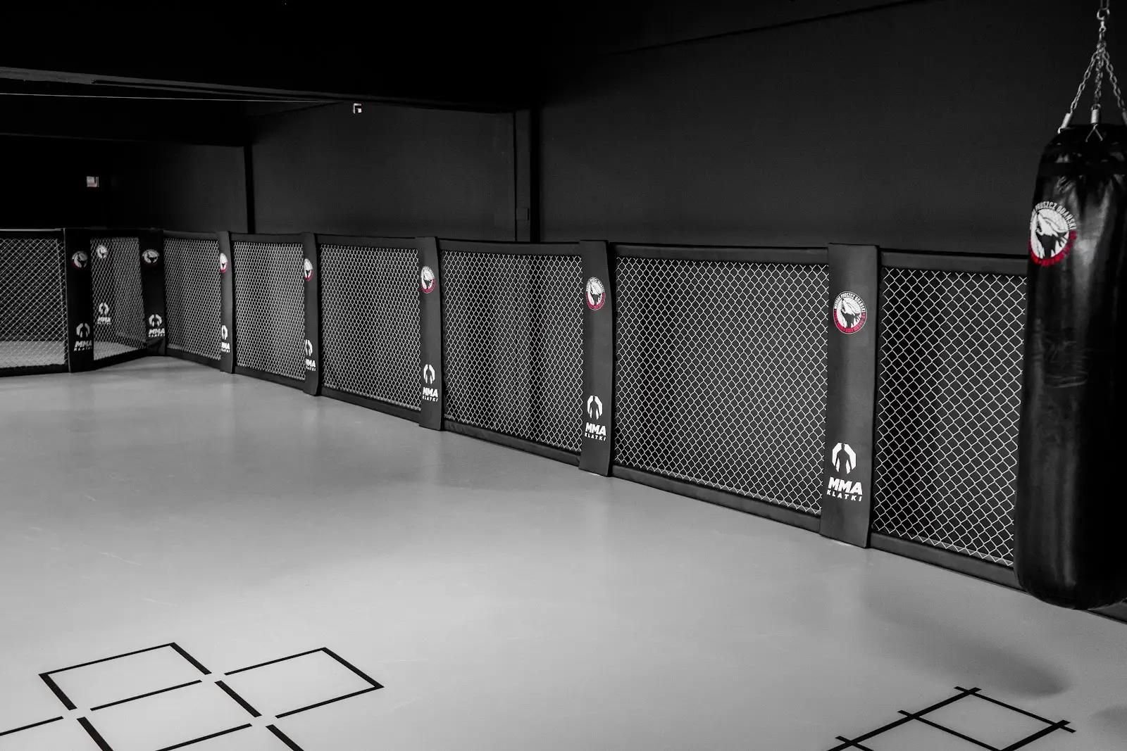 Długa ściana Cage Wall z logo klubu wzdłuż czarnej ściany, worek treningowy, szara mata z czarnymi polami koordynacyjnymi