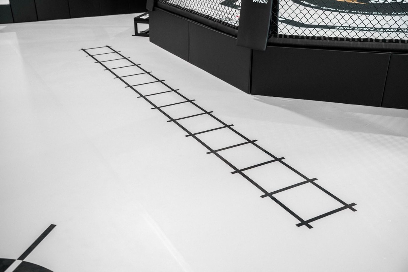 Drabinka footwork nadrukowana na macie przy podeście klatki MMA