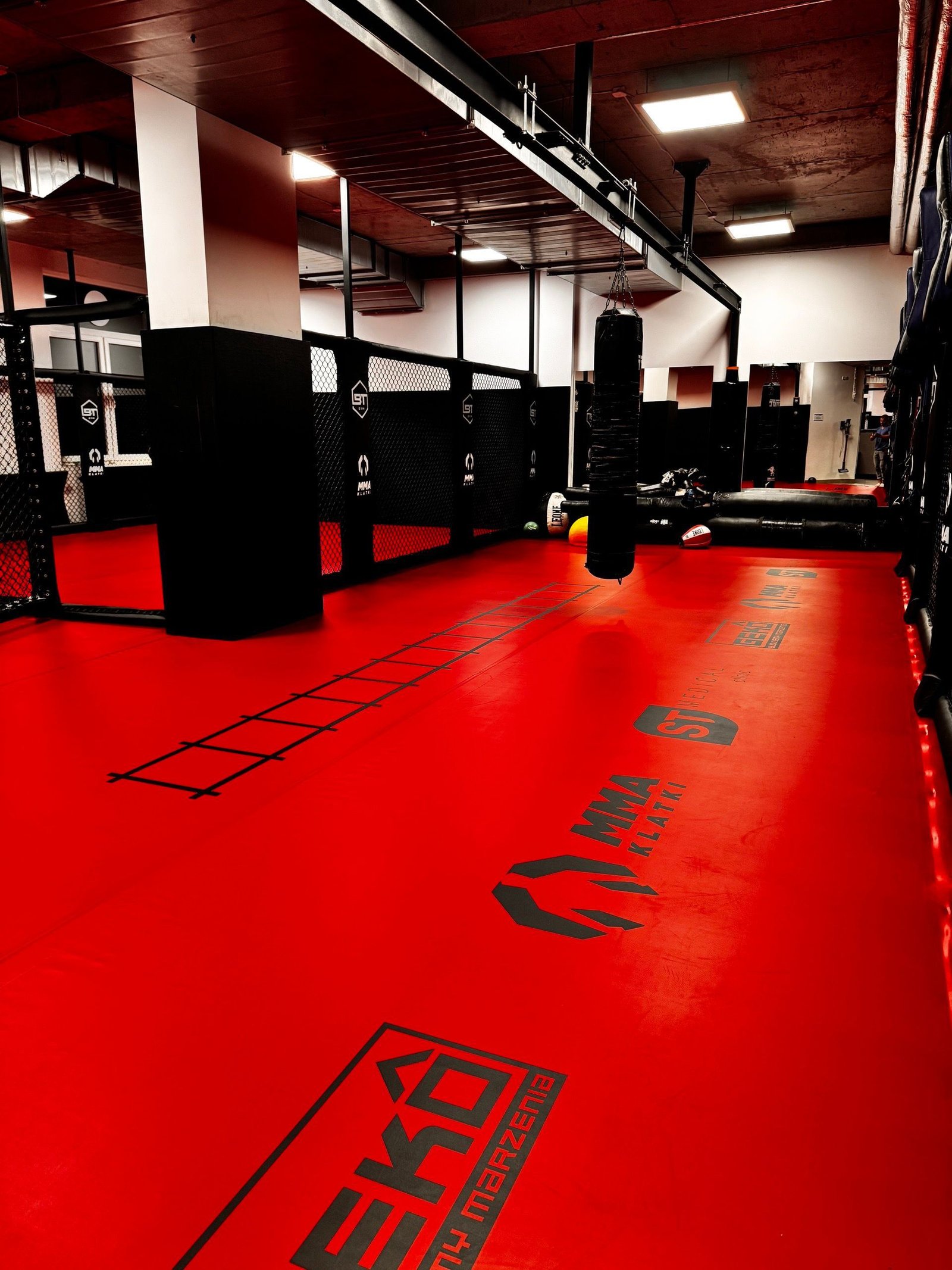 Strefa MMA BT Gym z czerwoną matą z drabinką koordynacyjną i workami bokserskimi