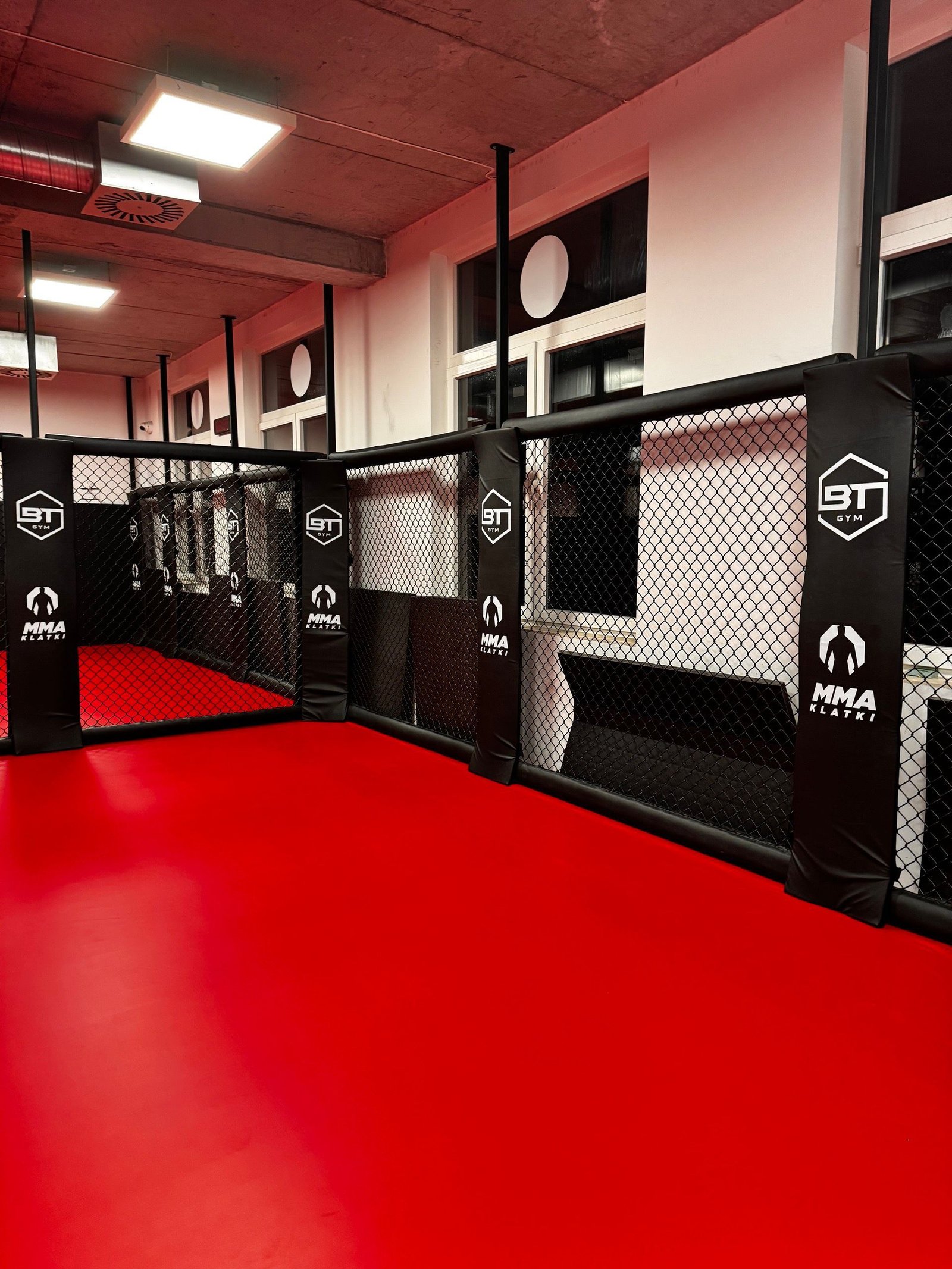 Panele klatki MMA z obszyciami z logo BT Gym przy czerwonej macie