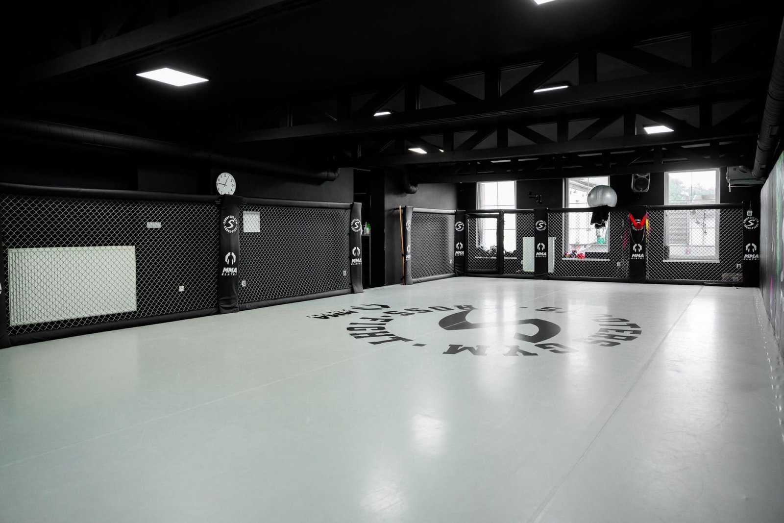 Centralne logo Shooters Gym Cross-Fight na jasnej macie przy workach bokserskich