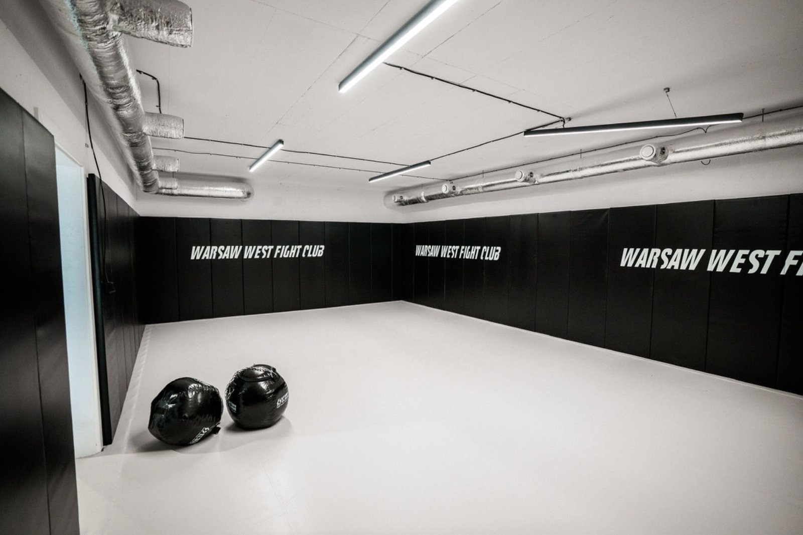 Mała sala treningowa z napisami Warsaw West Fight Club na czarnych matach ściennych
