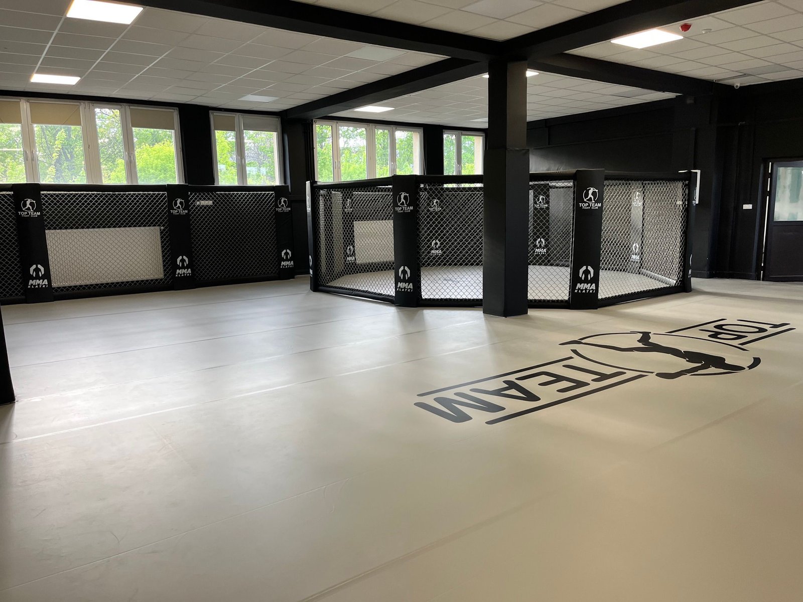 Główna sala Top Team Częstochowa z szarą matą z logo klubu i klatką MMA połączoną z systemem Cage Wall