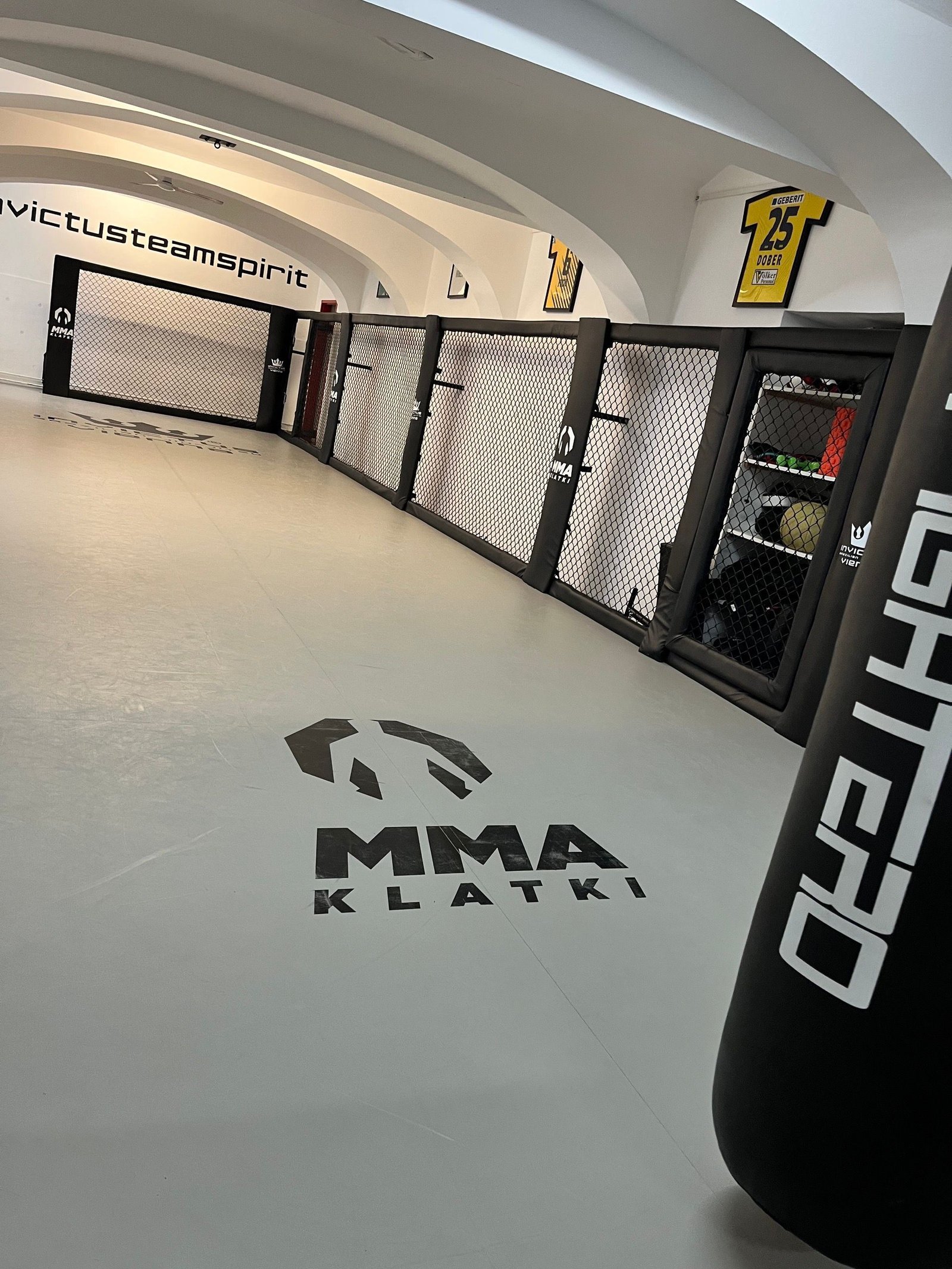Worek treningowy zawieszony przy ścianie Cage Wall obok półek na sprzęt w Invictus BJJ Vienna