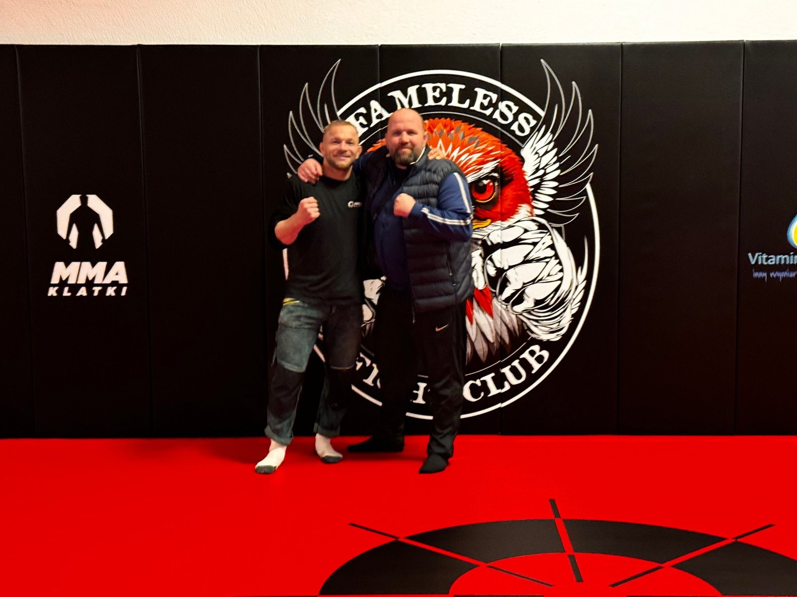 Dwaj mężczyźni na czerwonej macie przed logo Fameless Fight Club
