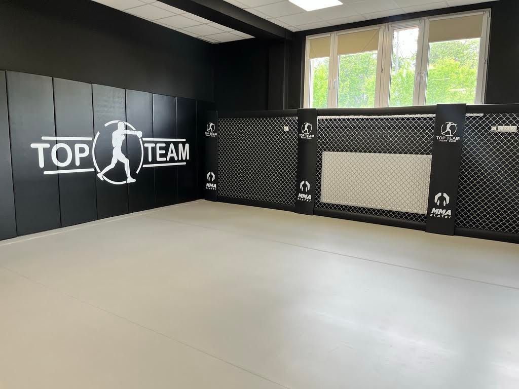 Czarne materace ścienne z logo klubu i niski panel Cage Wall pod oknem, beżowa mata w sali treningowej