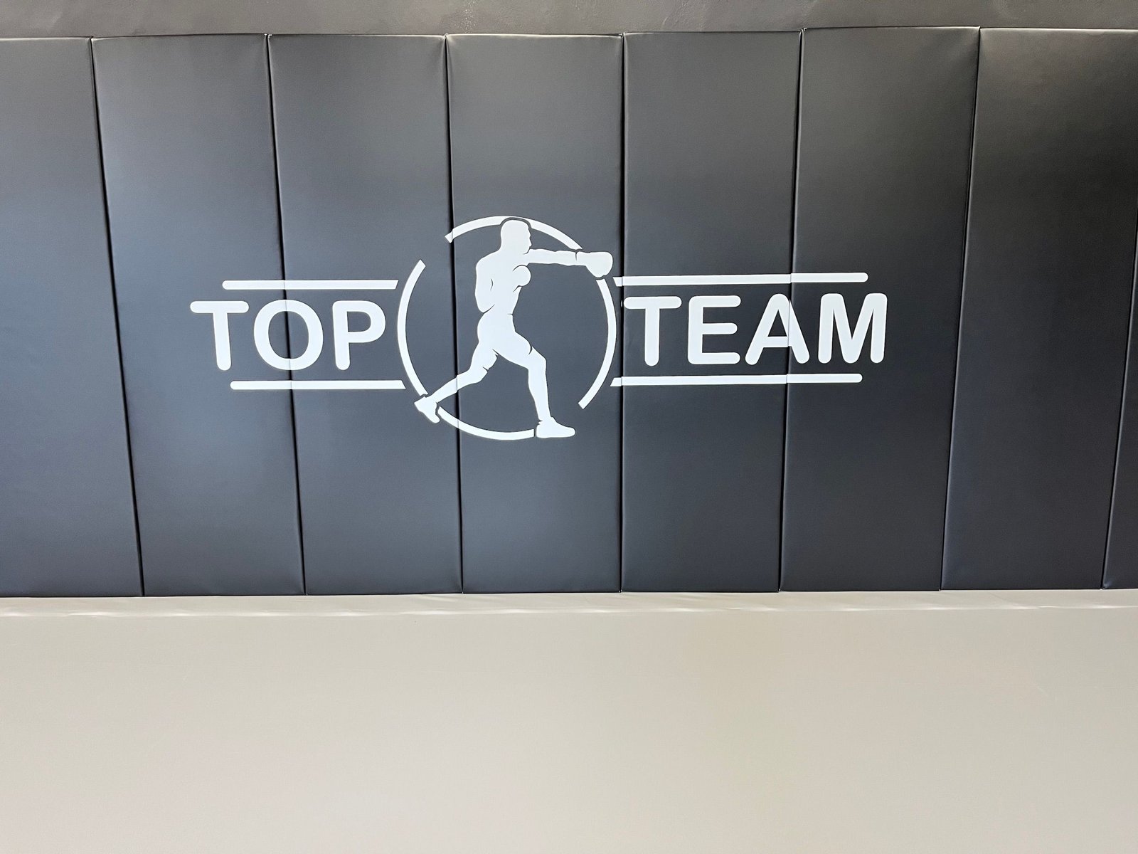 Logo Top Team na czarnych matach ściennych nad szarą matą podłogową