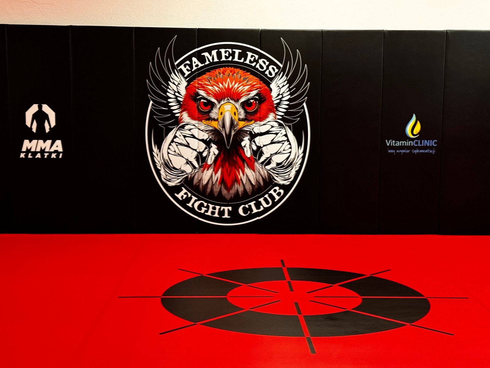 Logo Fameless Fight Club na czarnych matach ściennych nad kołem footwork