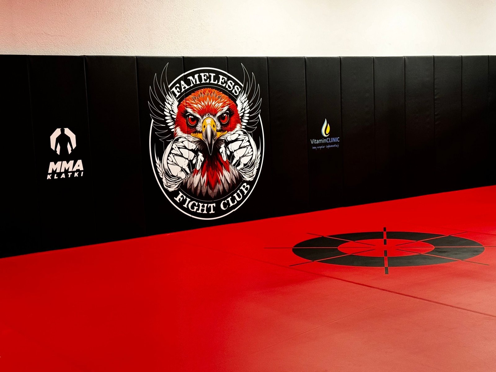 Czarne maty ścienne z logo Fameless Fight Club nad czerwoną matą z kołem do treningu footwork