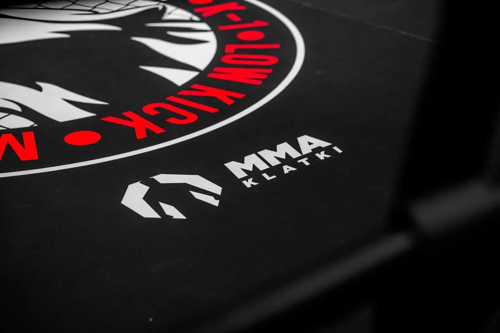 Zbliżenie czarnej maty z nadrukiem logo klubu i producenta, personalizowane wyposażenie sali MMA
