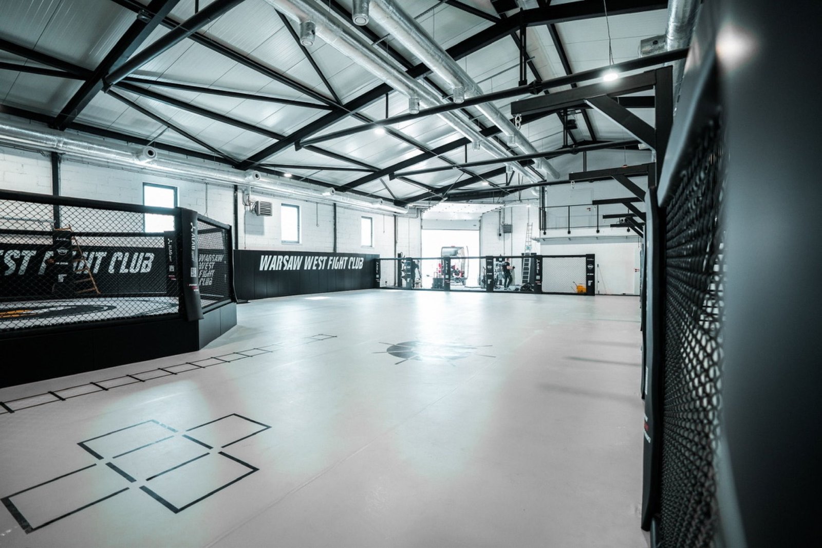 Główna hala Warsaw West Fight Club z klatką na podeście i jasną matą podłogową